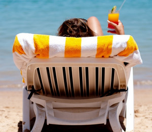 Девушка лежит на щезлонге на пляже с коктейлем в руке