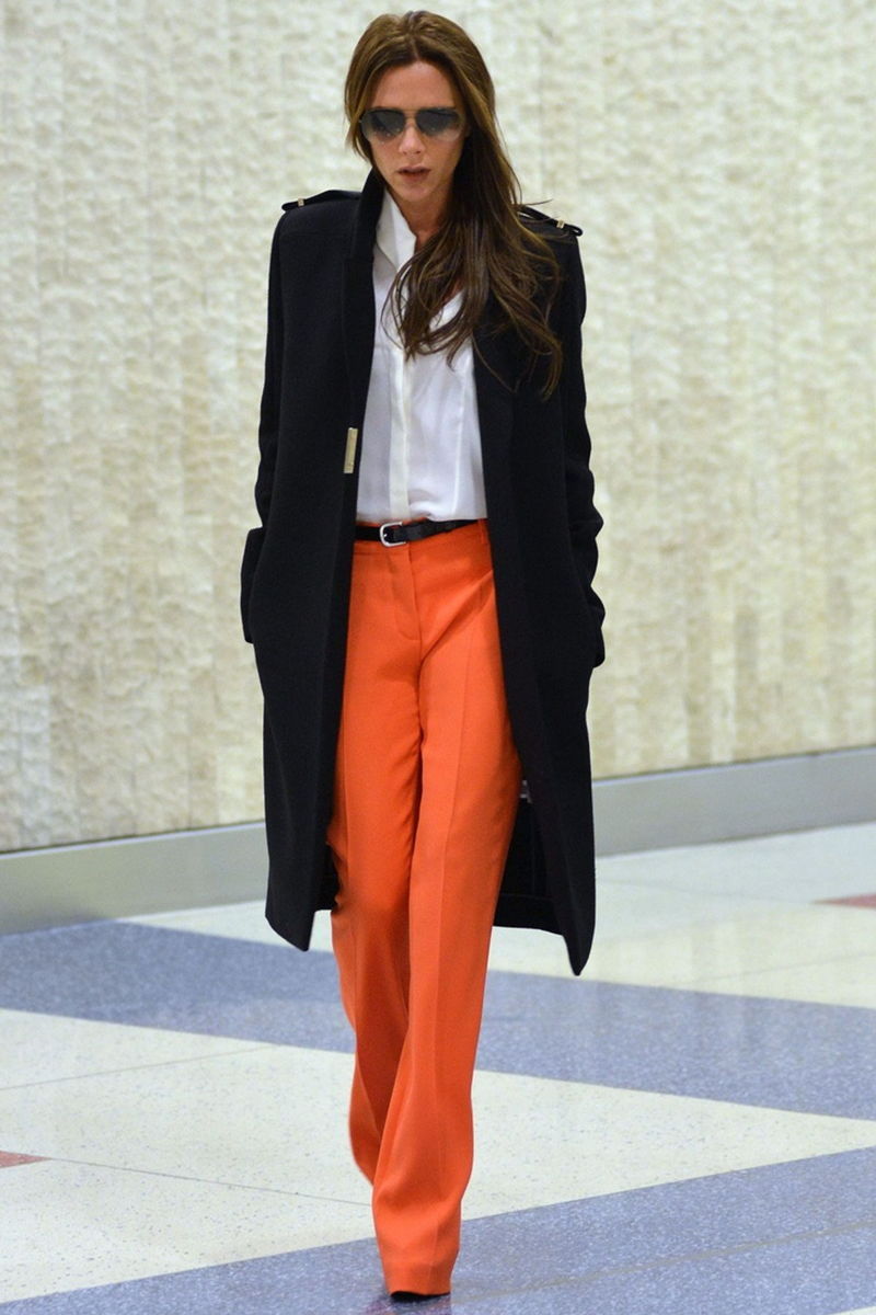 На фото: черное пальто. белая блуза и брюки оранжевого цвета.
