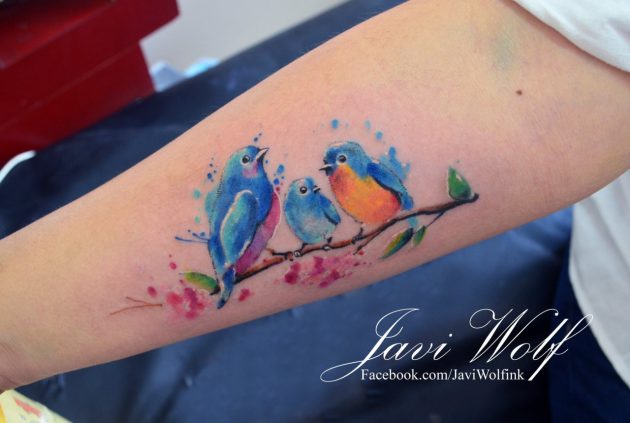 На фото: акварельная татуировка в виде ярких птиц на ветке.